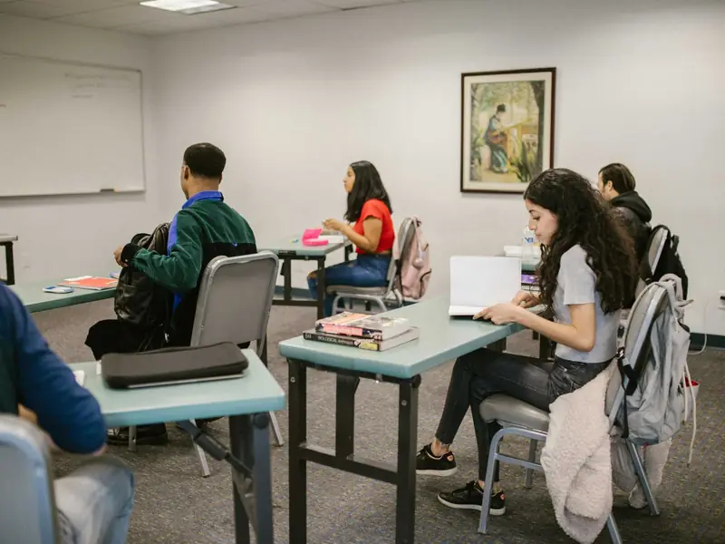 Alumnos adolescentes trabajando en pupitres individuales en un aula.
